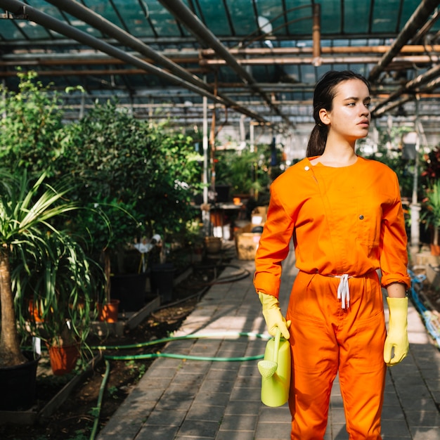 Young female gardener with watering can standing in greenhouse