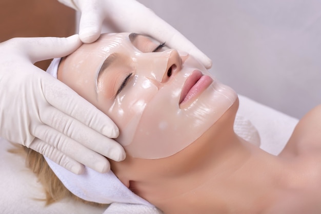 Young female getting skin mask treatment on her face with massage glove