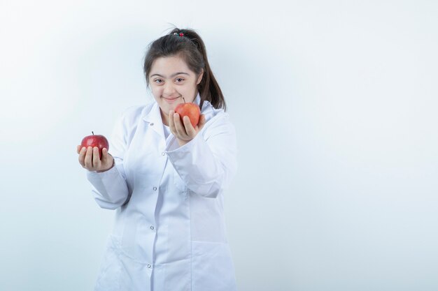 赤いリンゴの果実を保持している医者の制服を着た若い女性の女の子。