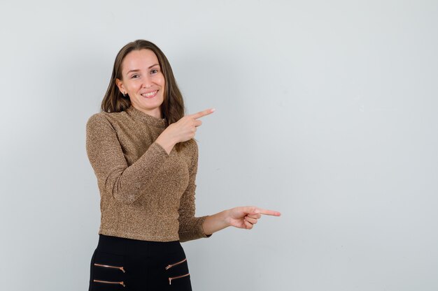 Young female in golden blouse pointing aside and looking merry , front view. space for text