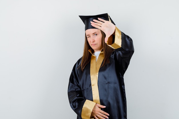 Молодая женщина-выпускница в академической одежде показывает жест стоп и выглядит уверенно, вид спереди.