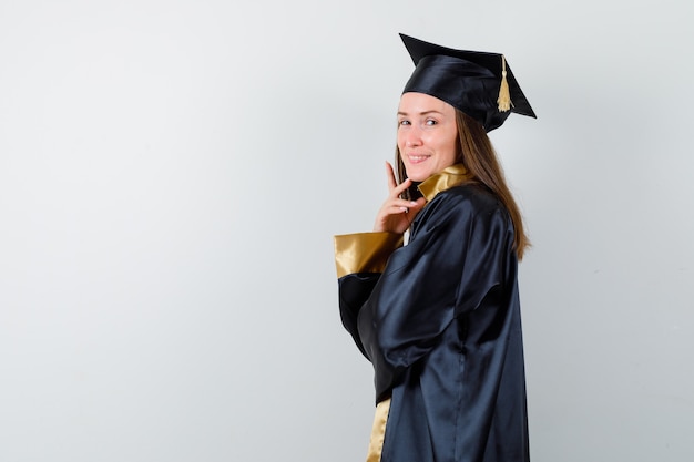 Молодая женщина-выпускница стоя позирует в академической одежде изолированы