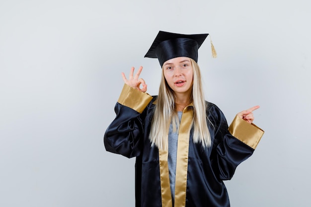 Free photo young female in graduate uniform pointing aside, showing ok gesture and looking confident