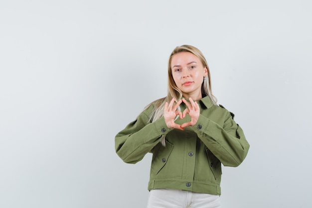 Giovane donna in giacca verde, jeans che mostrano gesto di pace e che sembra amabile, vista frontale.