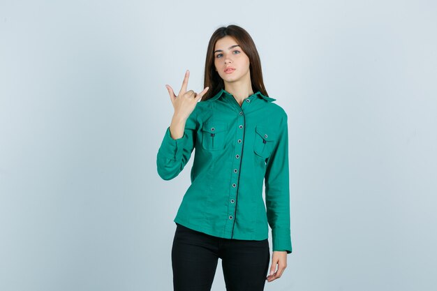Young female in green shirt, pants showing rock gesture and looking proud , front view.