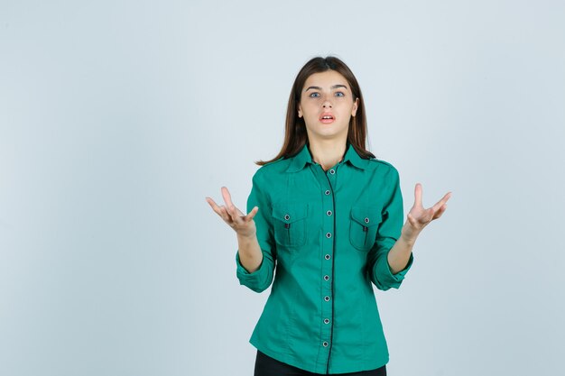 Young female in green shirt raising hands in aggressive manner and looking shocked , front view.