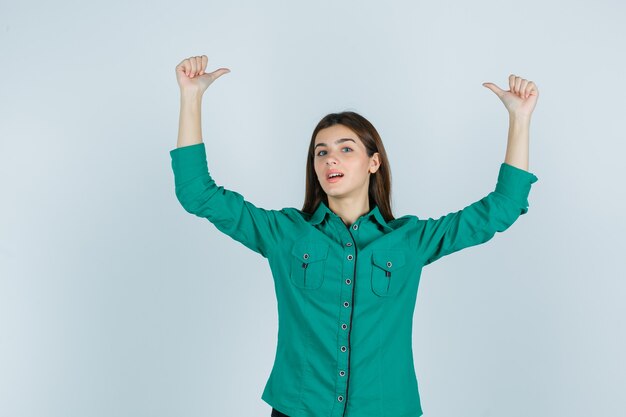 Young female in green shirt showing double thumbs up and looking confident , front view.