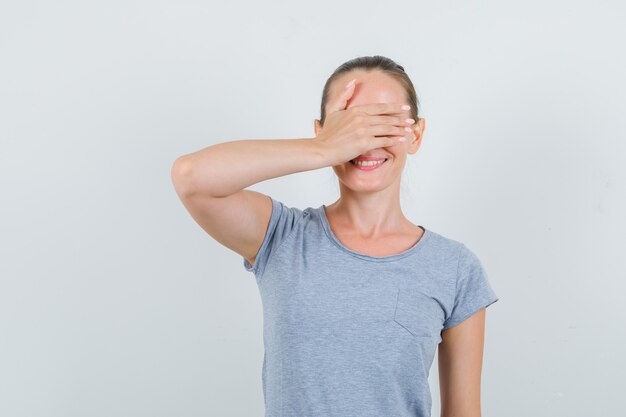 Young female in grey t-shirt holding hand on eyes and looking excited , front view.