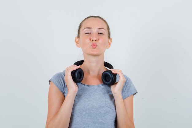 Free photo young female in grey t-shirt keeping lips rounded and holding headphones , front view.