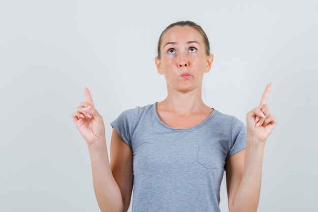 Young female in grey t-shirt pointing up and looking focused , front view.