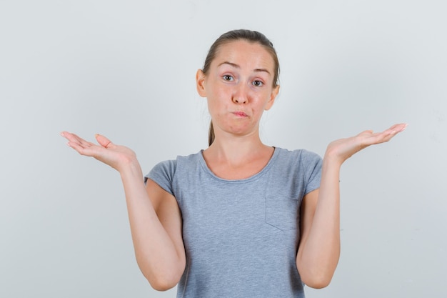 Young female in grey t-shirt showing helpless gesture and looking confused , front view.