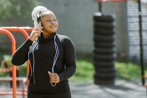 屋外でのトレーニングを楽しんでいる若い女性。スポーティな人々のライフスタイルのコンセプト。スマートフォンを持っているスポーツウェアの女性