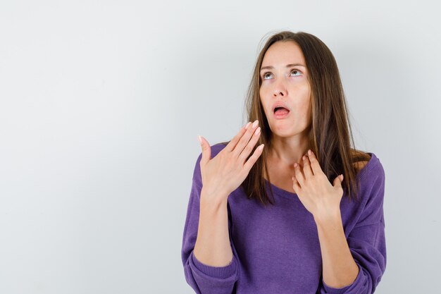 Young female having sore throat in violet shirt and looking beloved. front view.