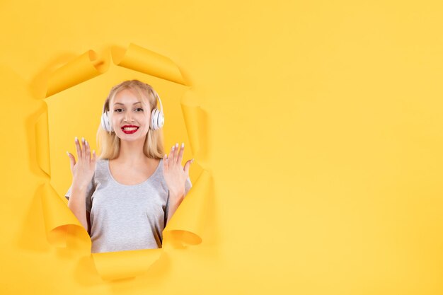 Young female in headphones on torn yellow paper background audio sound music