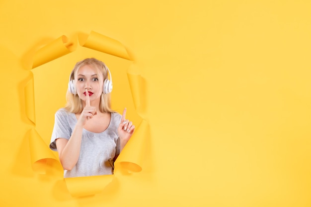 Young female in headphones on torn yellow paper background audio ultrasound sound