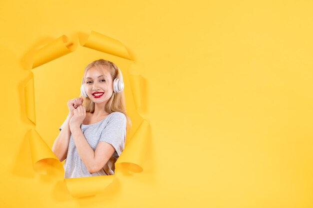 Young female in headphones on torn yellow paper background ultrasound sound music