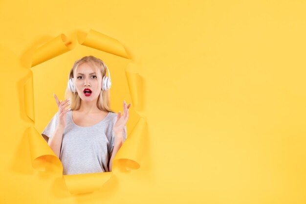 Young female in headphones on torn yellow paper surface