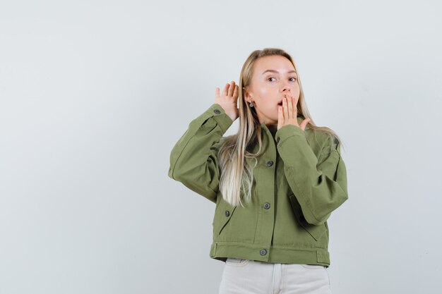 Young female hearing something in green jacket and looking surprised. front view.