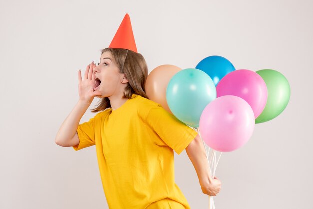 彼女の背中の後ろにカラフルな風船を隠している若い女性は白を求めています