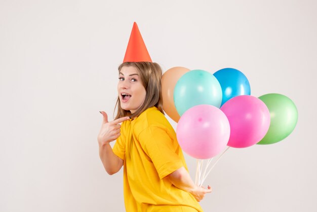 young female hiding colorful balloons behind her back on white