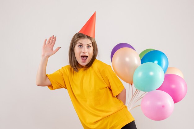 young female hiding colorful balloons behind her back on white