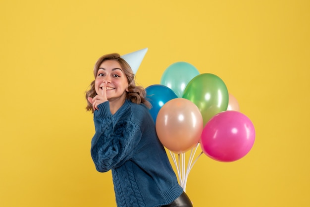 Giovane femmina nascondendo palloncini colorati dietro la schiena su giallo