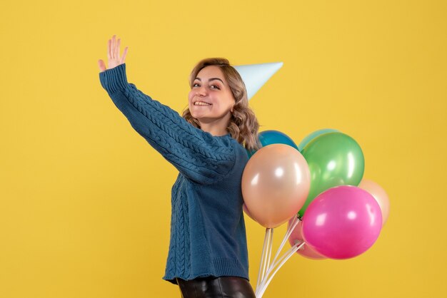 young female hiding colorful balloons behind her back on yellow