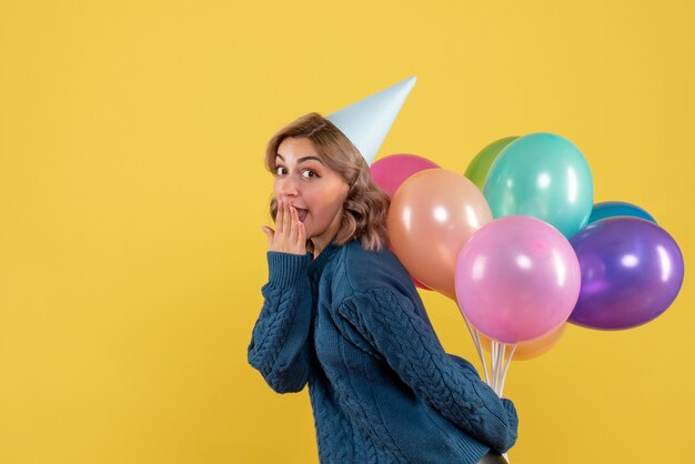 young female hiding colorful balloons behind her back on yellow