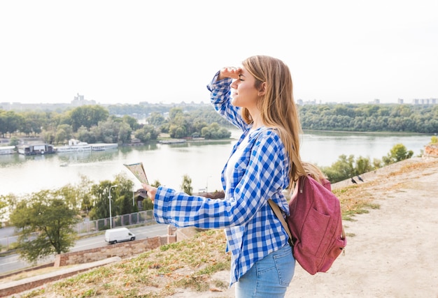 Young female hiker with map shielding her eyes at outdoors