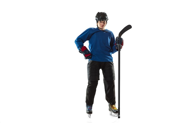 Young female hockey player with the stick on ice court and white wall. Sportswoman wearing equipment and helmet posing. Concept of sport, healthy lifestyle, motion, action, human emotions.