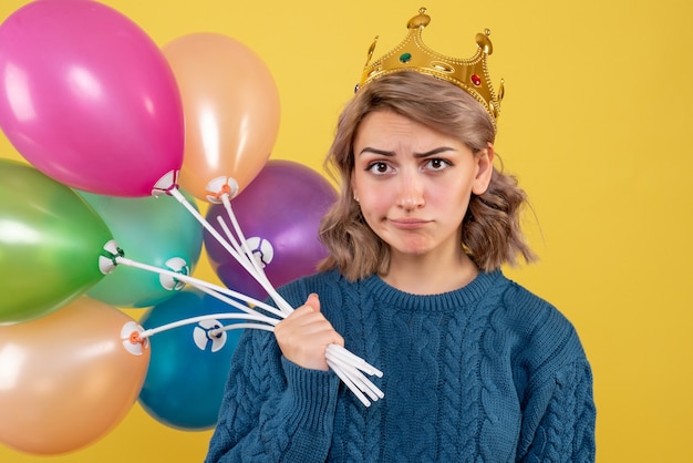 Free photo young female holding balloons in crown on yellow