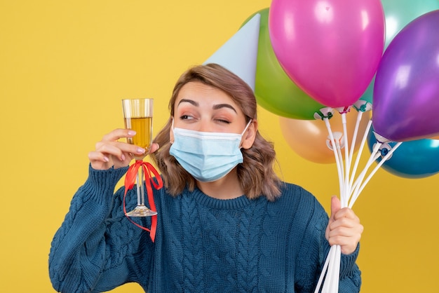 young female holding balloons and glass of champagne on yellow