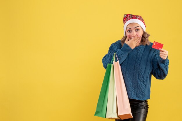 young female holding bank card and packages after shopping on yellow