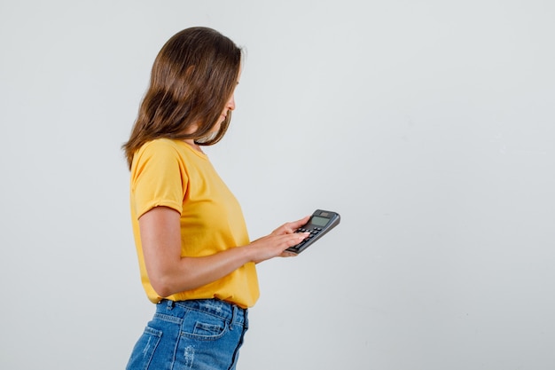 Молодая женщина, держащая калькулятор в футболке, шортах.