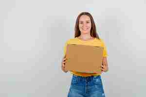 Free photo young female holding cardboard box and smiling in t-shirt, shorts