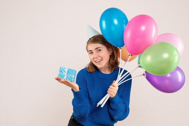 young female holding colorful balloons and little present on white