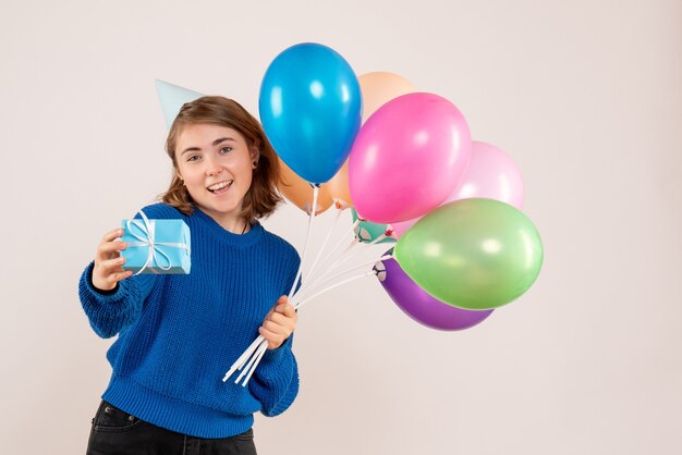 молодая женщина держит разноцветные воздушные шары и маленький подарок на белом