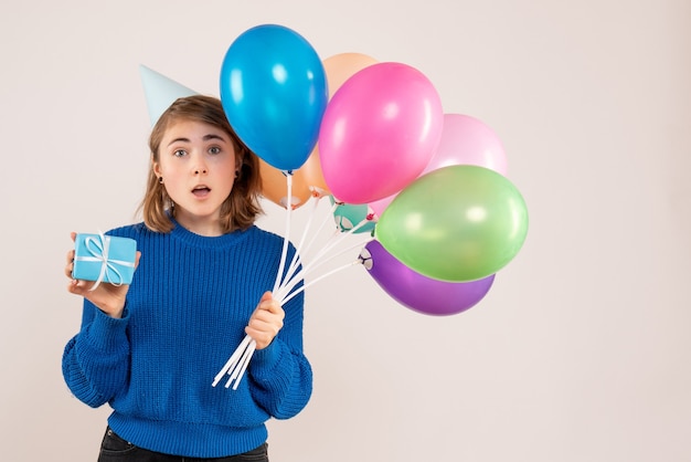 молодая женщина держит разноцветные воздушные шары и маленький подарок на белом