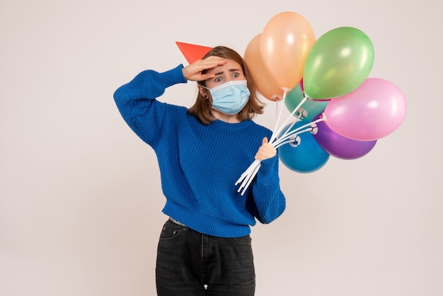 young female holding colorful balloons in mask on white