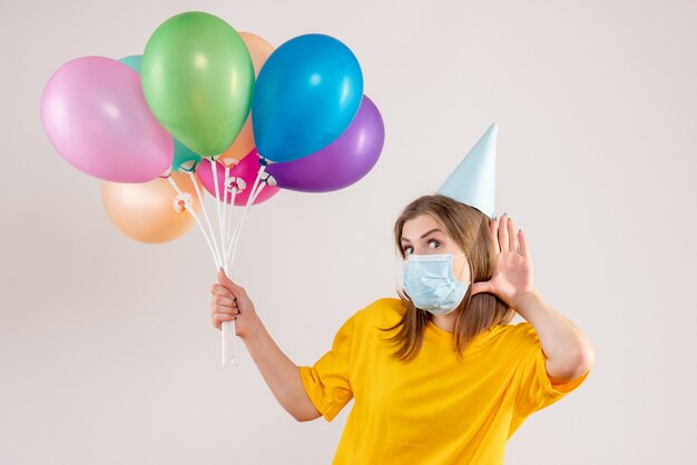 young female holding colorful balloons in mask on white