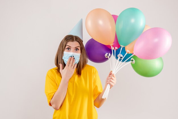 young female holding colorful balloons in mask on white