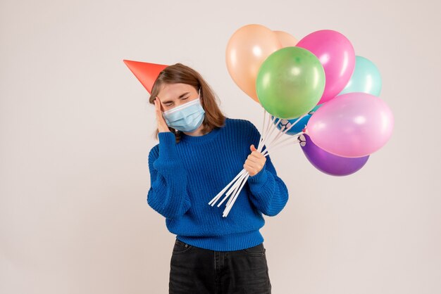 白のマスクでカラフルな風船を保持している若い女性