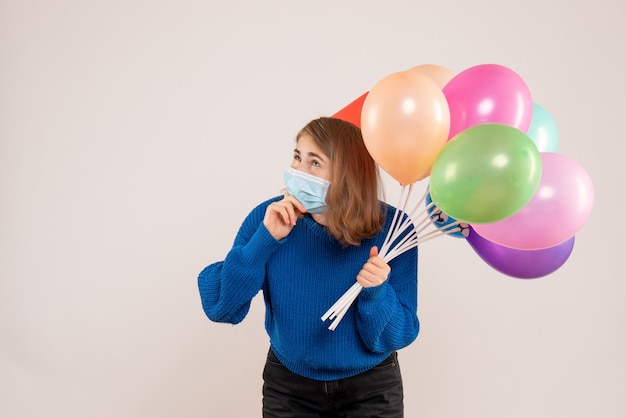 young female holding colorful balloons in mask on white