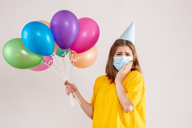 Giovane donna in possesso di palloncini colorati in maschera su bianco