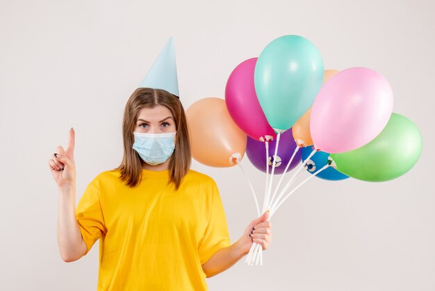 young female holding colorful balloons in mask on white