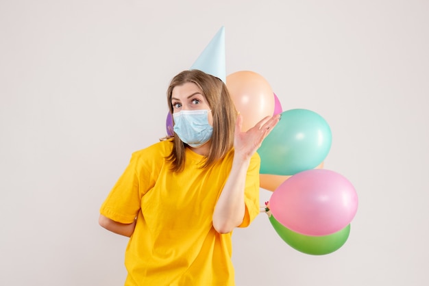 young female holding colorful balloons in mask on white