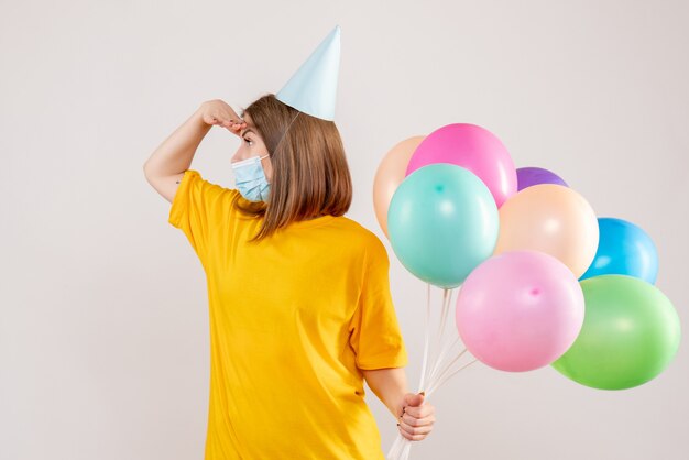 young female holding colorful balloons in mask on white