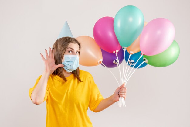 young female holding colorful balloons in mask on white