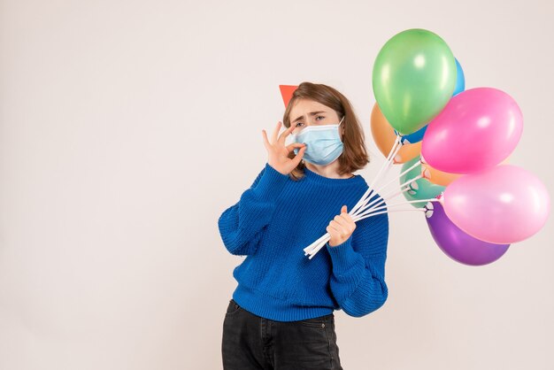 young female holding colorful balloons in mask on white