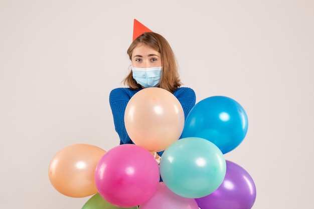 young female holding colorful balloons in mask on white